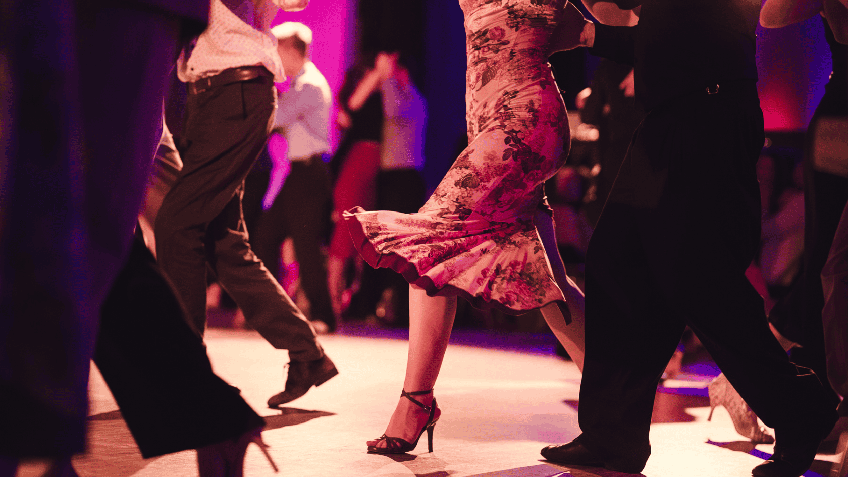 Dancers moving together at a Tango Flow Milonga Baviera in Munich under warm pink and red lights.